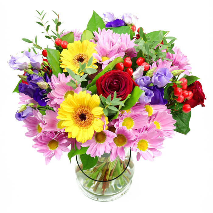 A striking mixed bouquet stands proudly in a clear glass vase against a bright white backdrop, allowing each colour and texture to shine with the clarity of daylight streaming through Barbican high-rise windows. The arrangement is opulent yet balanced, its central focus a cluster of deep red roses whose velvety petals spiral open in layered whorls, suggesting affection, gratitude, or quiet celebration. Sharing the spotlight are bold yellow gerbera daisies, their wide petals surrounding dark, warm brown centres that give a strong, graphic contrast, much like artwork displayed in the Barbican Centre. Around these larger blooms, soft pink chrysanthemums, similar to daisies, spread in generous bundles. Their numerous delicate petals and petite yellow centres create a feathery ring of pastel colour that softens the whole design. Interspersed throughout are graceful stems of purple and lavender lisianthus, with bell-shaped, sometimes partially opened flowers that bring in cool, soothing tones and a sense of modern elegance. Nestled among the petals, glossy red hypericum berries punctuate the bouquet with small, rounded forms, adding a layer of tactile interest and a subtle, festive note. Surrounding all these blooms, various shades of fresh green foliage-from deep, broad leaves to lighter, airy sprigs-provide structure and a natural frame, evoking the planted terraces and pockets of greenery that soften the Barbican's concrete lines. Through the clear glass vase, the viewer can see the cleanly trimmed stems standing in transparent water, a testament to the florist's precision and emphasis on freshness. The overall mood of the bouquet feels warm, contemporary, and generous, making it a beautiful choice for a dinner table in a Barbican flat, a thoughtful office gesture on London Wall, or a congratulatory surprise after a performance nearby.